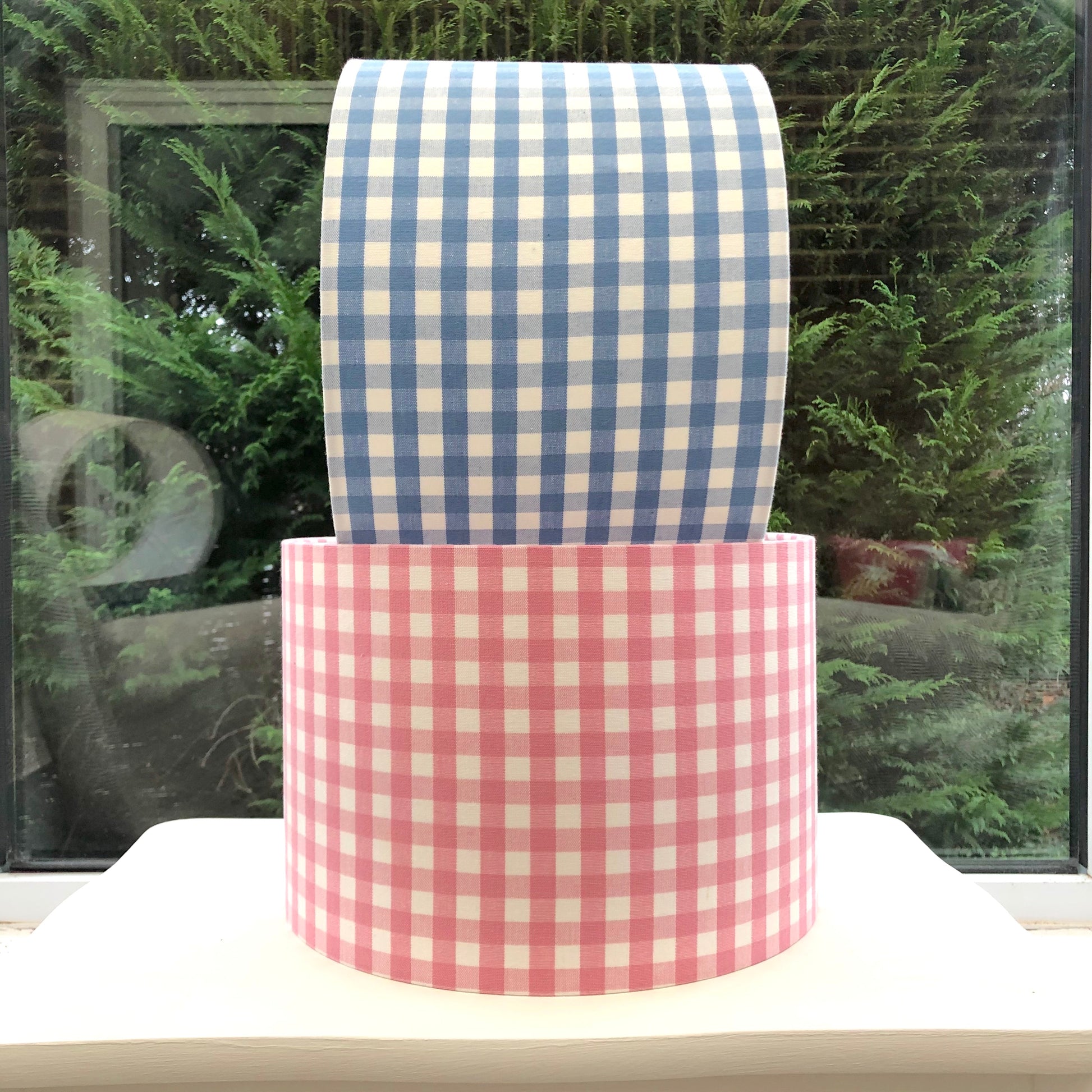 Two charming gingham lampshades in blue and pink, featuring a classic checked pattern, adding a playful and cozy touch to any room decor.