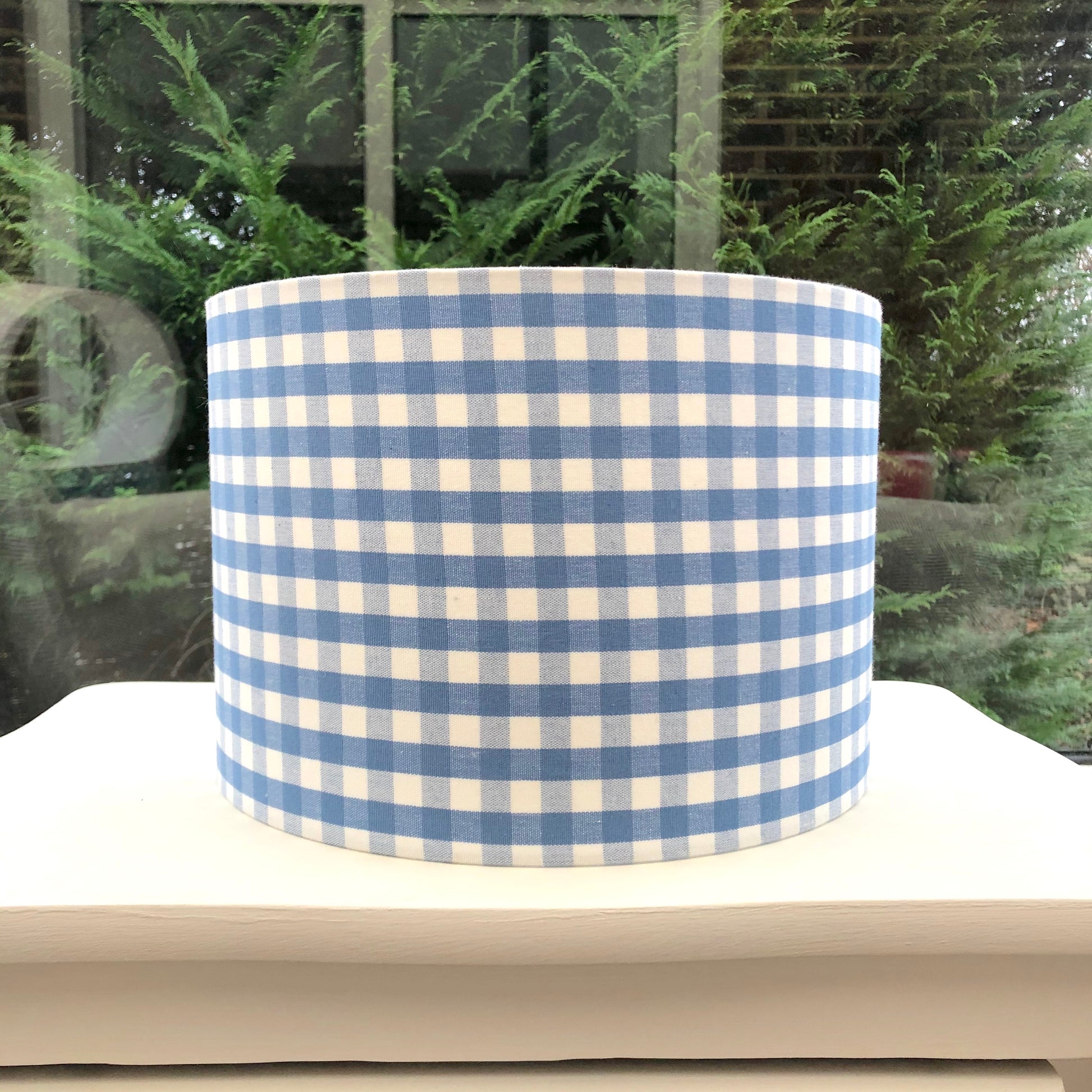 A charming blue gingham patterned lampshade with a classic checkered design, perfect for adding a touch of rustic charm to any room.