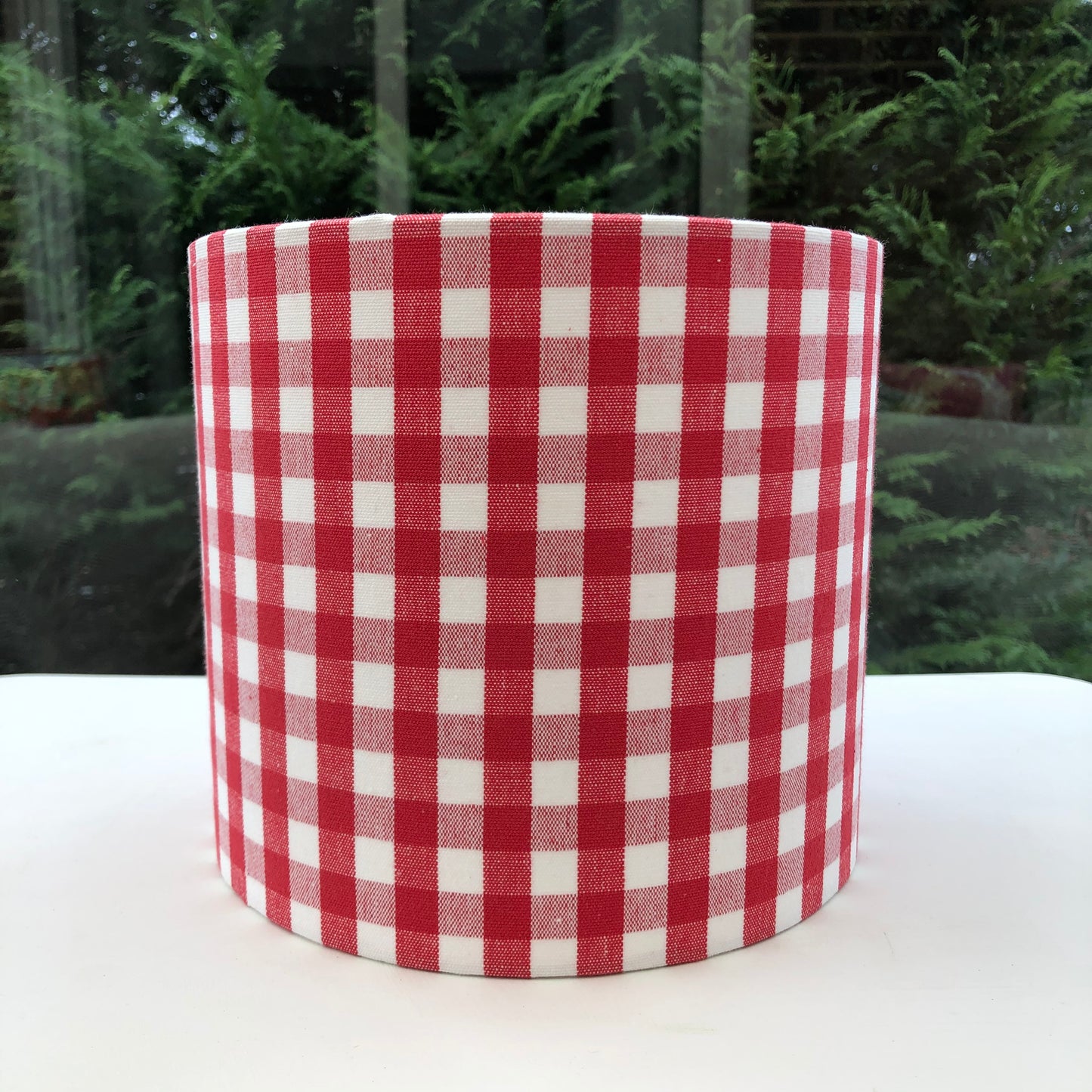 Bright red coloured gingham-patterned lampshade, adding a touch of rustic charm to any space.