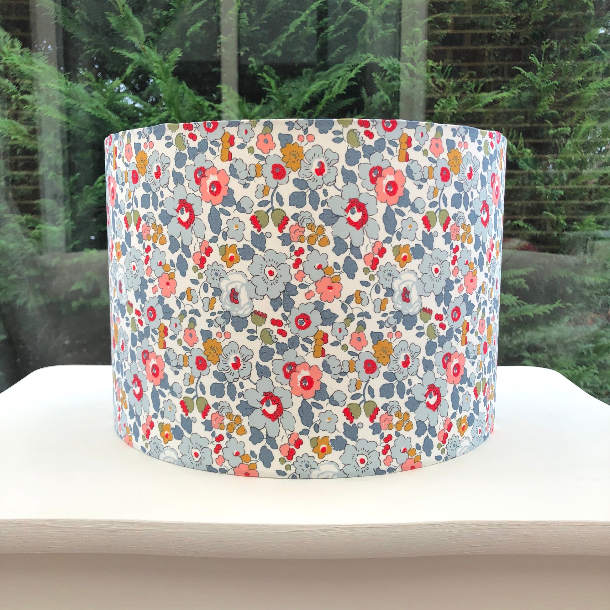 Charming grey lampshade with delicate, multicolored floral patterns in shades of pink, blue, and yellow, designed to bring a touch of whimsy and elegance to any room.