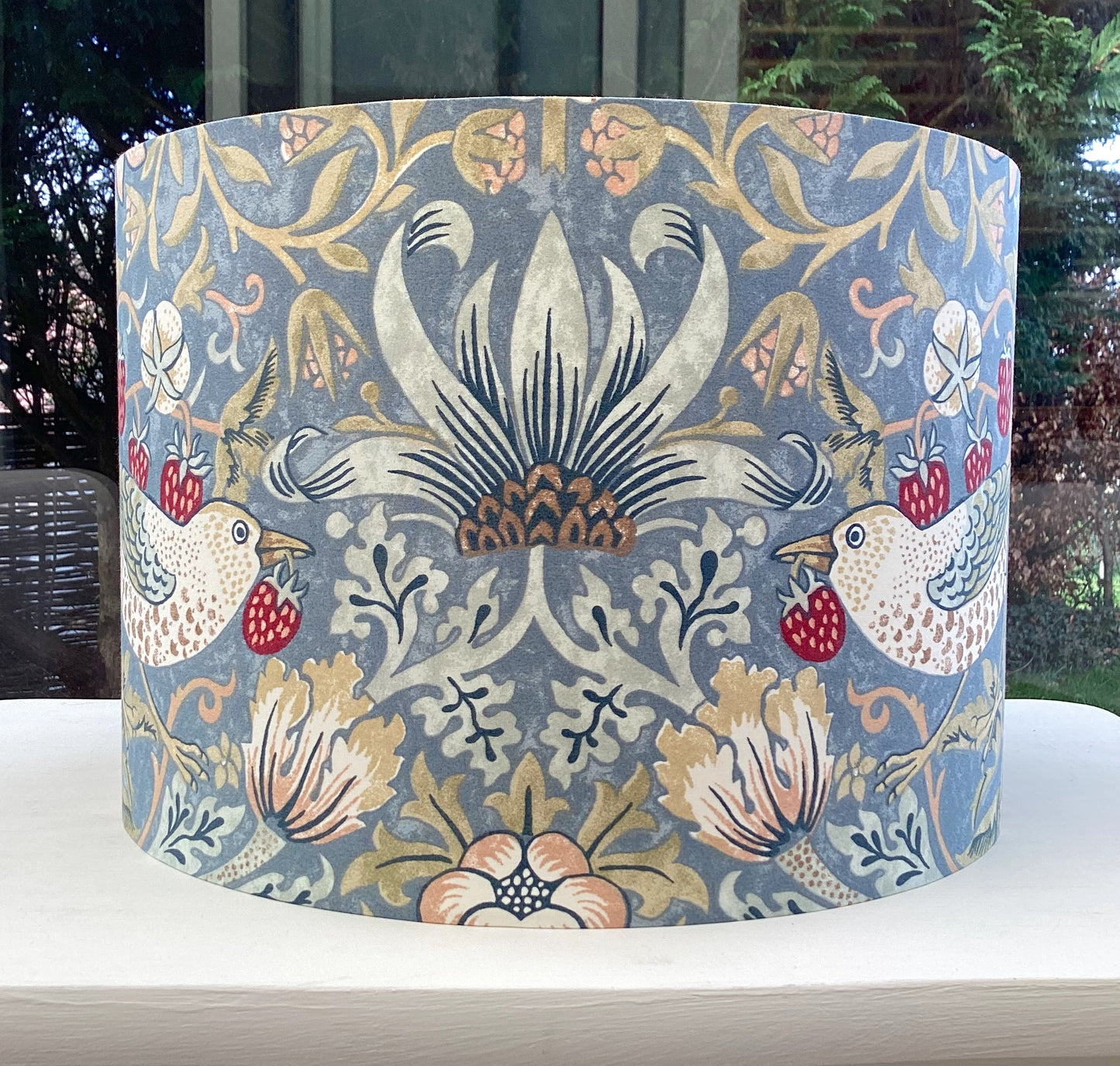 A vibrant cool slate blue lampshade with intricate William Morris patterns, illuminated from within, casting a warm and inviting glow.