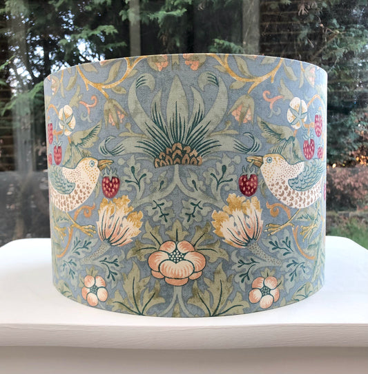 A vibrant cool slate blue lampshade with intricate William Morris patterns, illuminated from within, casting a warm and inviting glow.