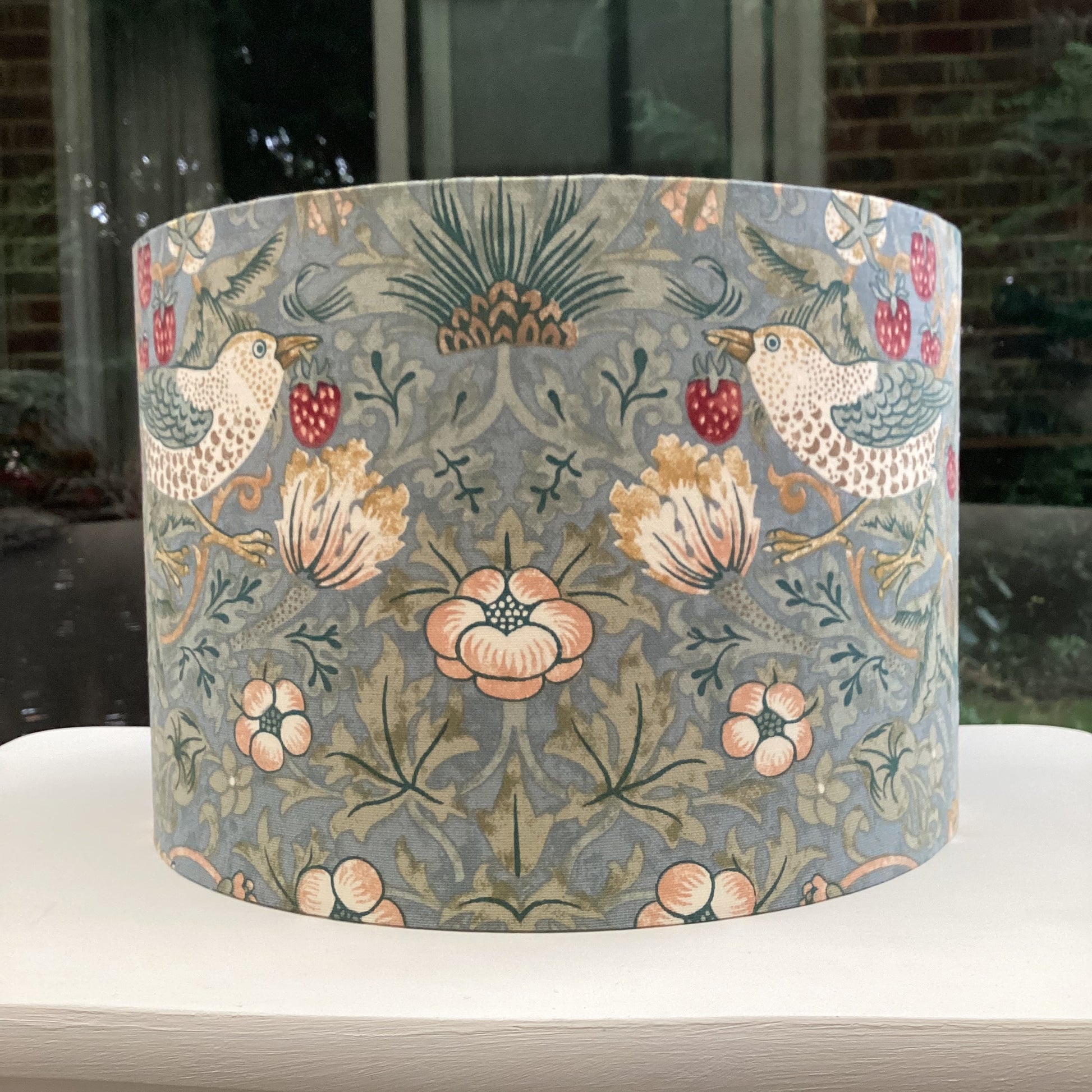 A vibrant cool slate blue lampshade with intricate William Morris patterns, illuminated from within, casting a warm and inviting glow.