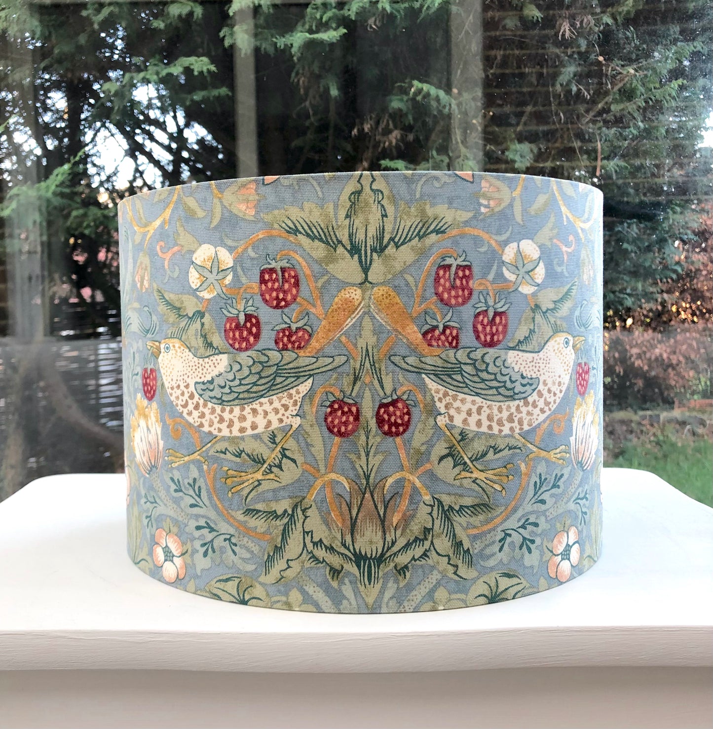 A vibrant cool slate blue lampshade with intricate William Morris patterns, illuminated from within, casting a warm and inviting glow.