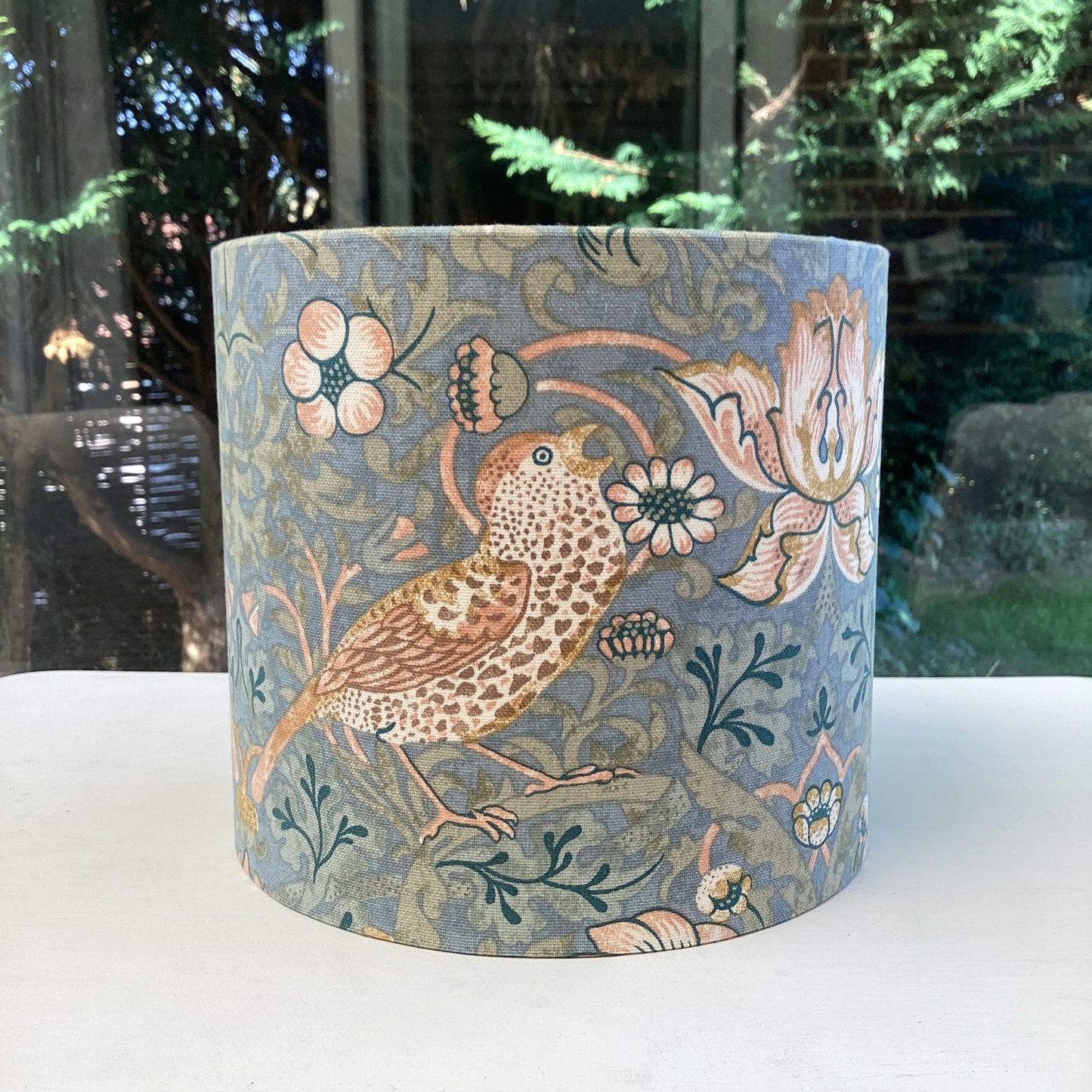 A vibrant cool slate blue lampshade with intricate William Morris patterns, illuminated from within, casting a warm and inviting glow.