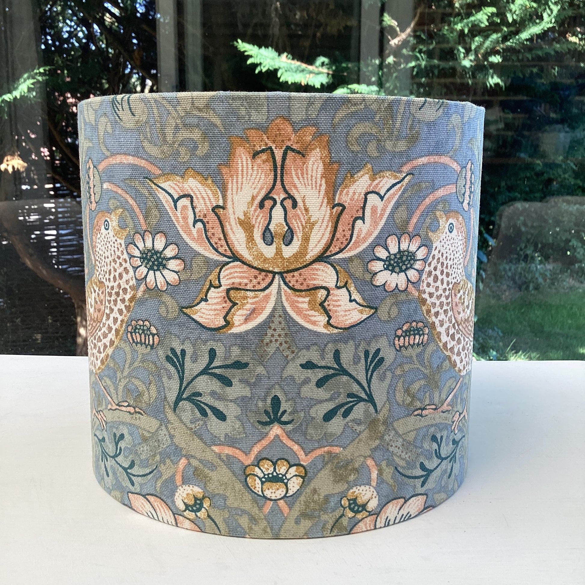 A vibrant cool slate blue lampshade with intricate William Morris patterns, illuminated from within, casting a warm and inviting glow.