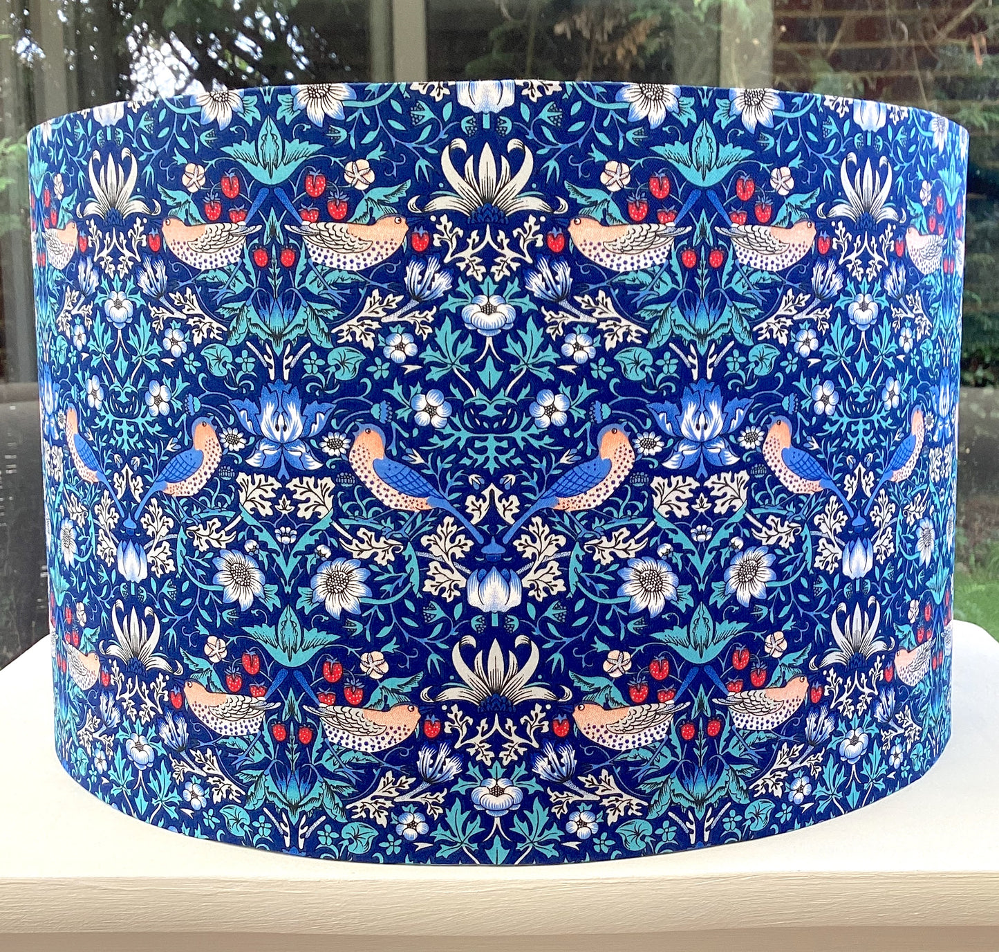 Bright blue coloured lampshade featuring a traditional strawberry thief pattern, creating a cozy atmosphere with its soft glow.