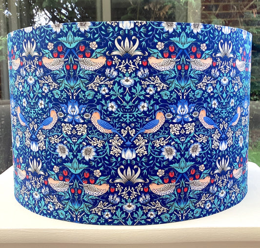 Bright blue coloured lampshade featuring a traditional strawberry thief pattern, creating a cozy atmosphere with its soft glow.