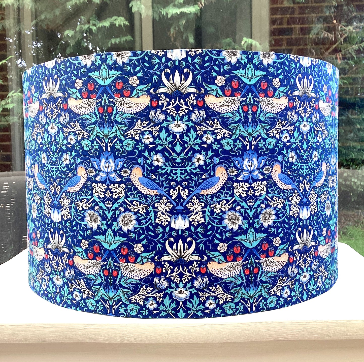 Bright blue coloured lampshade featuring a traditional strawberry thief pattern, creating a cozy atmosphere with its soft glow.