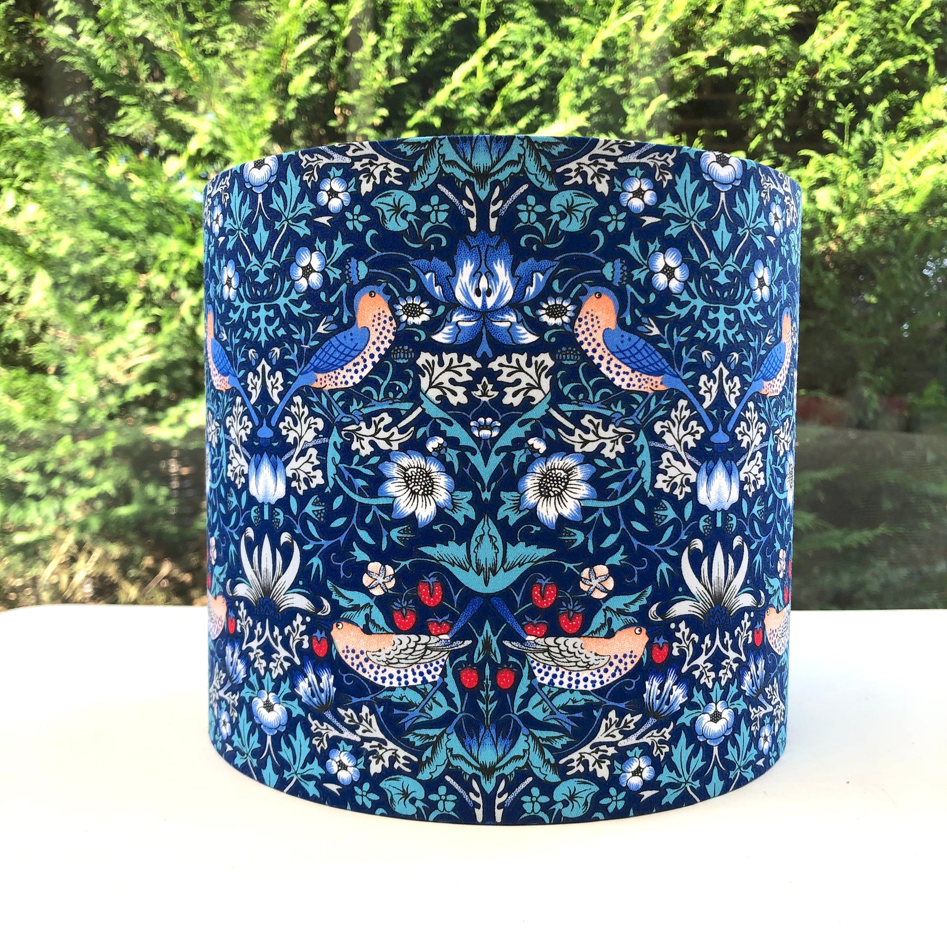 Bright blue coloured lampshade featuring a traditional strawberry thief pattern, creating a cozy atmosphere with its soft glow.