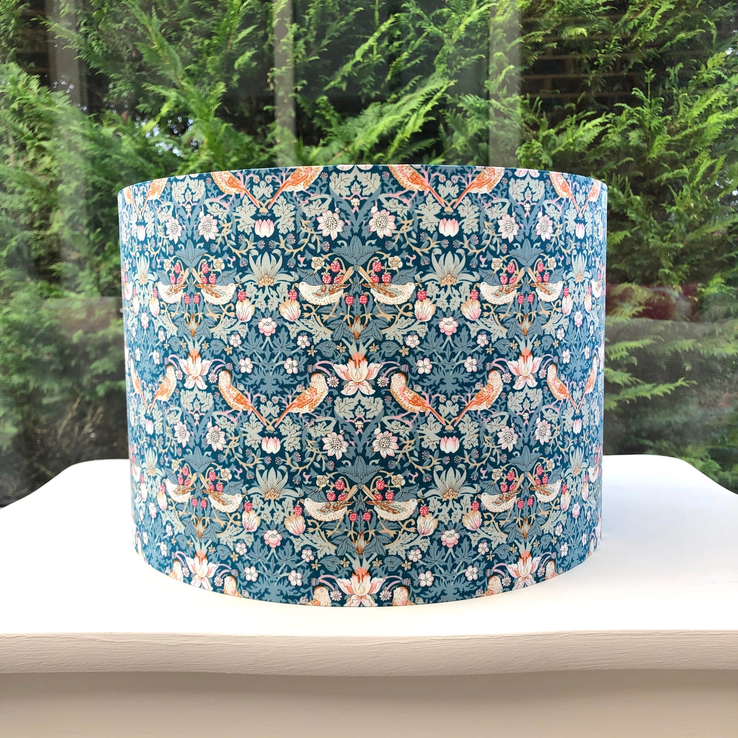 A vibrant green blue lampshade with intricate William Morris patterns, illuminated from within, casting a warm and inviting glow.