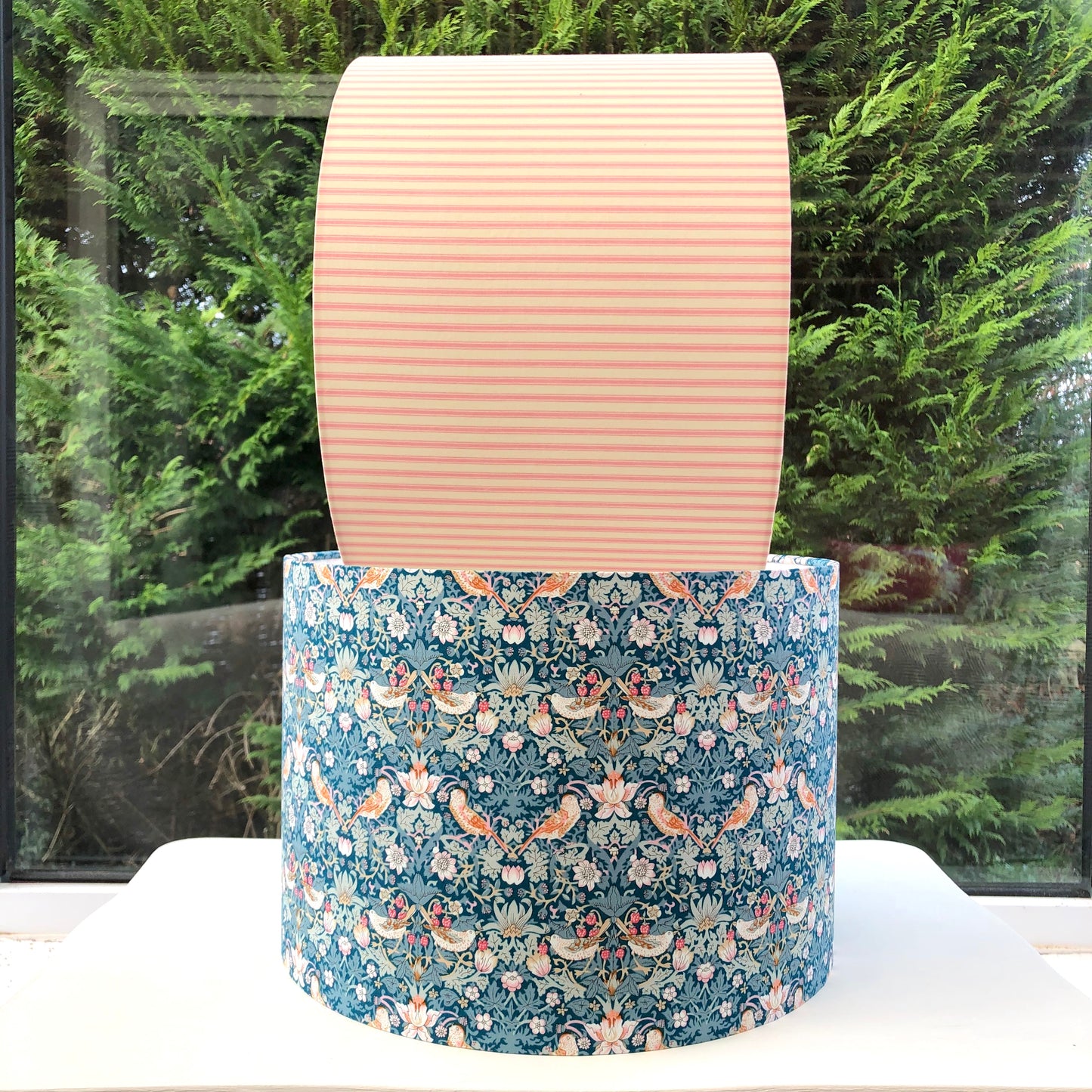 A vibrant green blue lampshade with intricate William Morris patterns, illuminated from within, casting a warm and inviting glow.