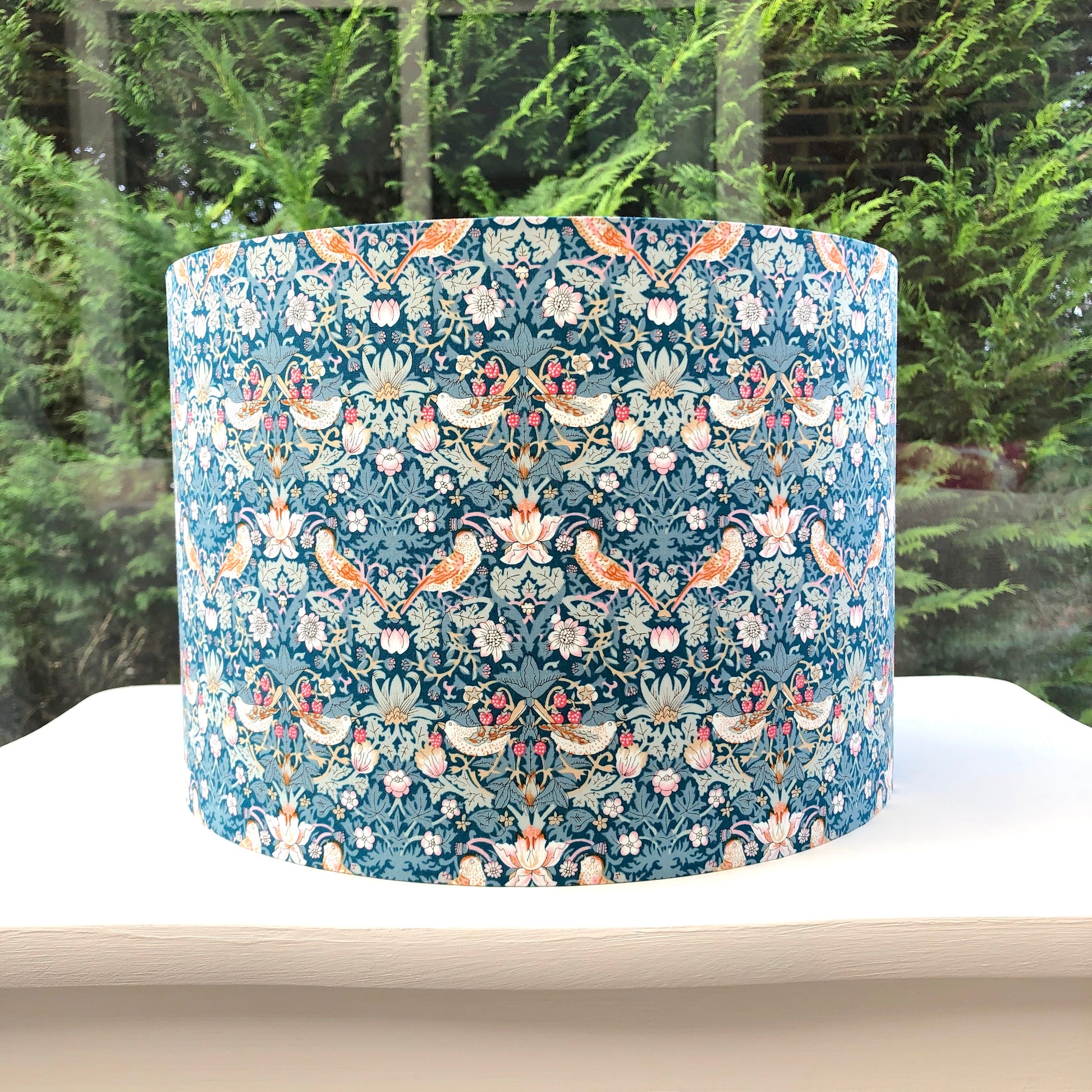 A vibrant green blue lampshade with intricate William Morris patterns, illuminated from within, casting a warm and inviting glow.