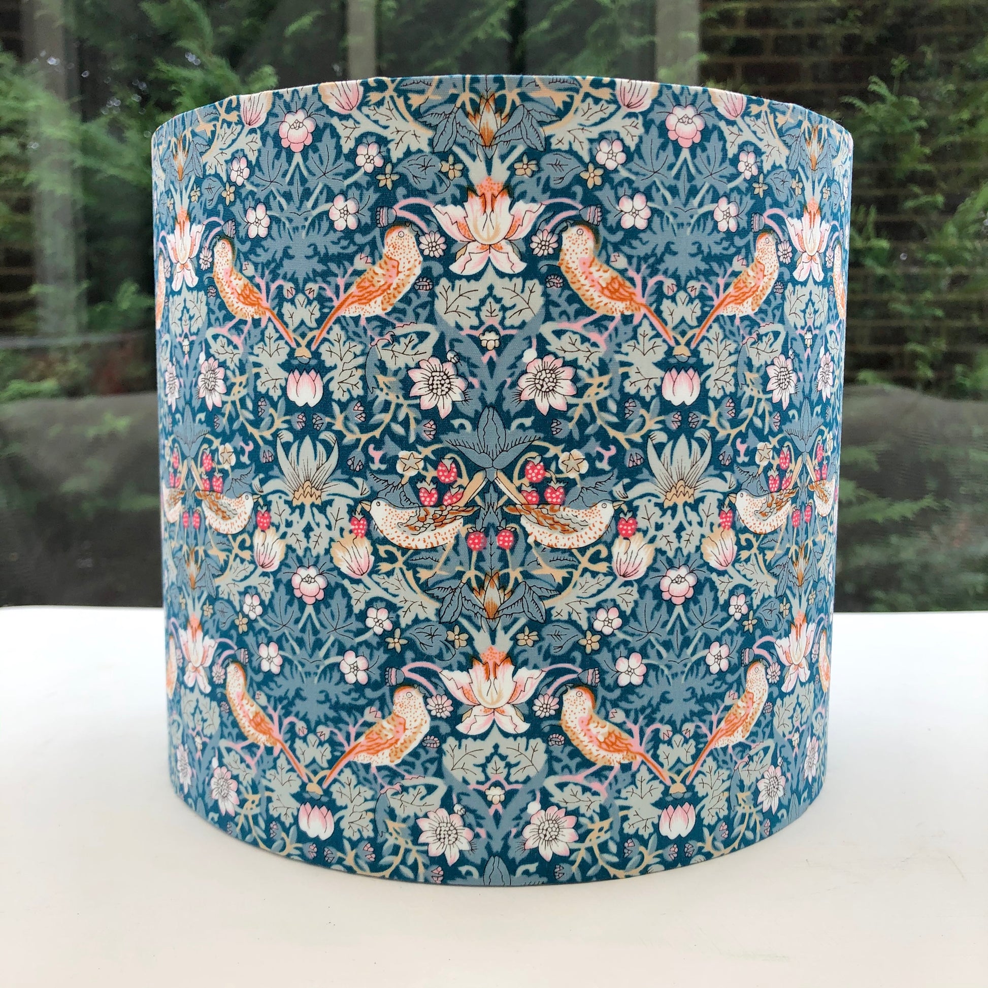 A vibrant green blue lampshade with intricate William Morris patterns, illuminated from within, casting a warm and inviting glow.