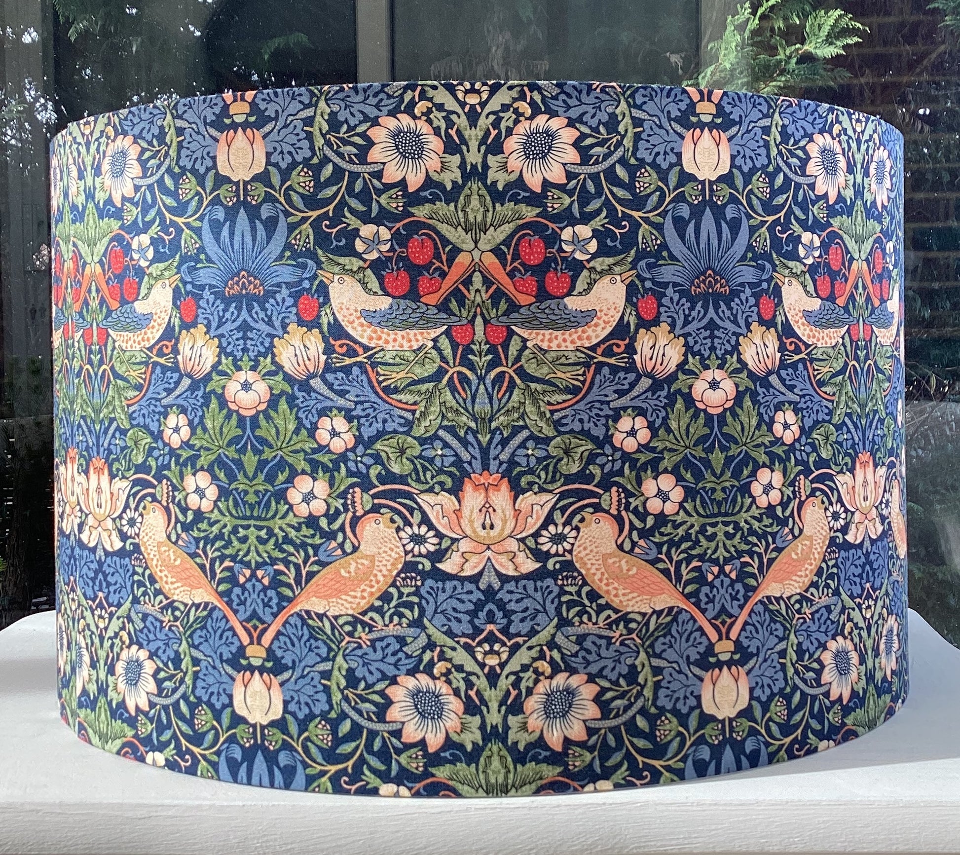 A vibrant navy blue lampshade with intricate William Morris patterns, illuminated from within, casting a warm and inviting glow.