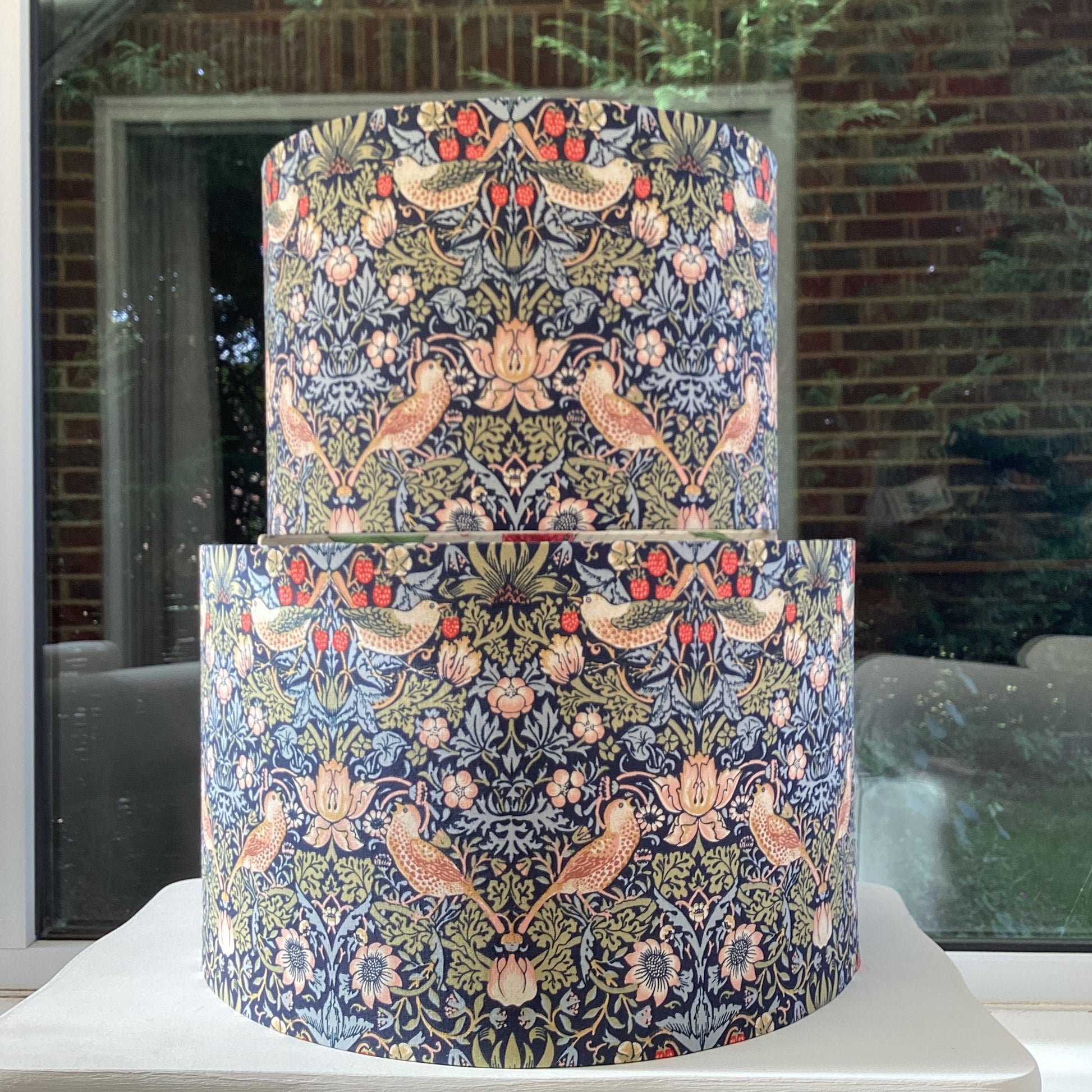 A vibrant navy blue lampshade with intricate William Morris patterns, illuminated from within, casting a warm and inviting glow.