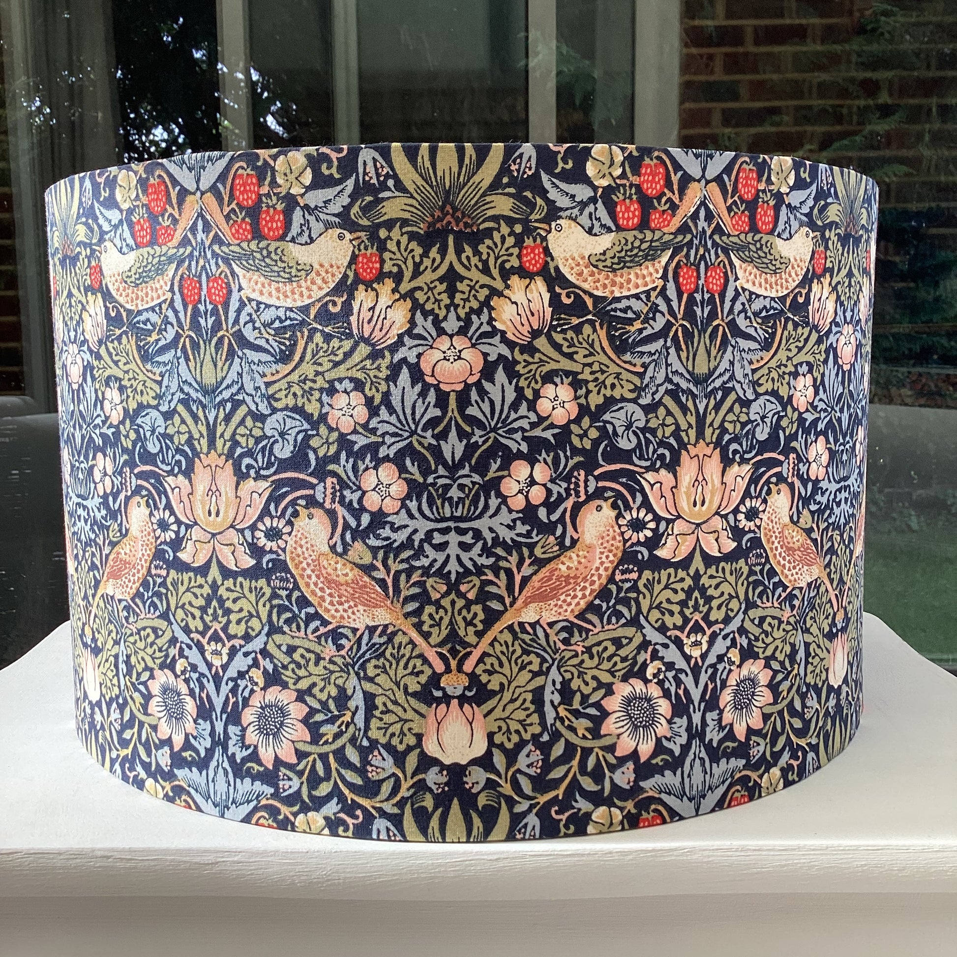 A vibrant navy blue lampshade with intricate William Morris patterns, illuminated from within, casting a warm and inviting glow.