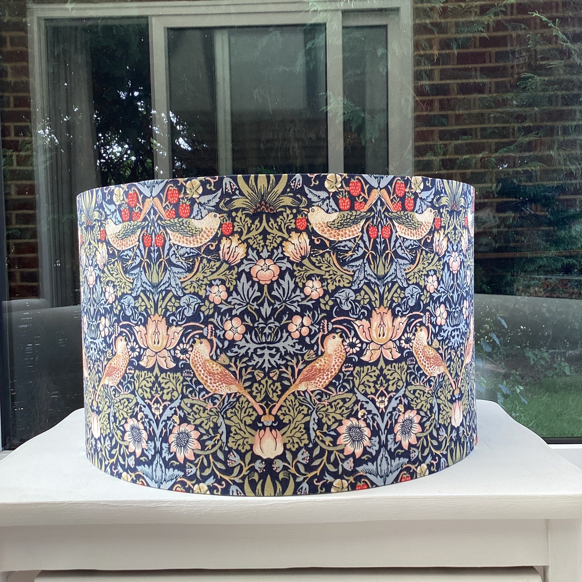 A vibrant navy blue lampshade with intricate William Morris patterns, illuminated from within, casting a warm and inviting glow.