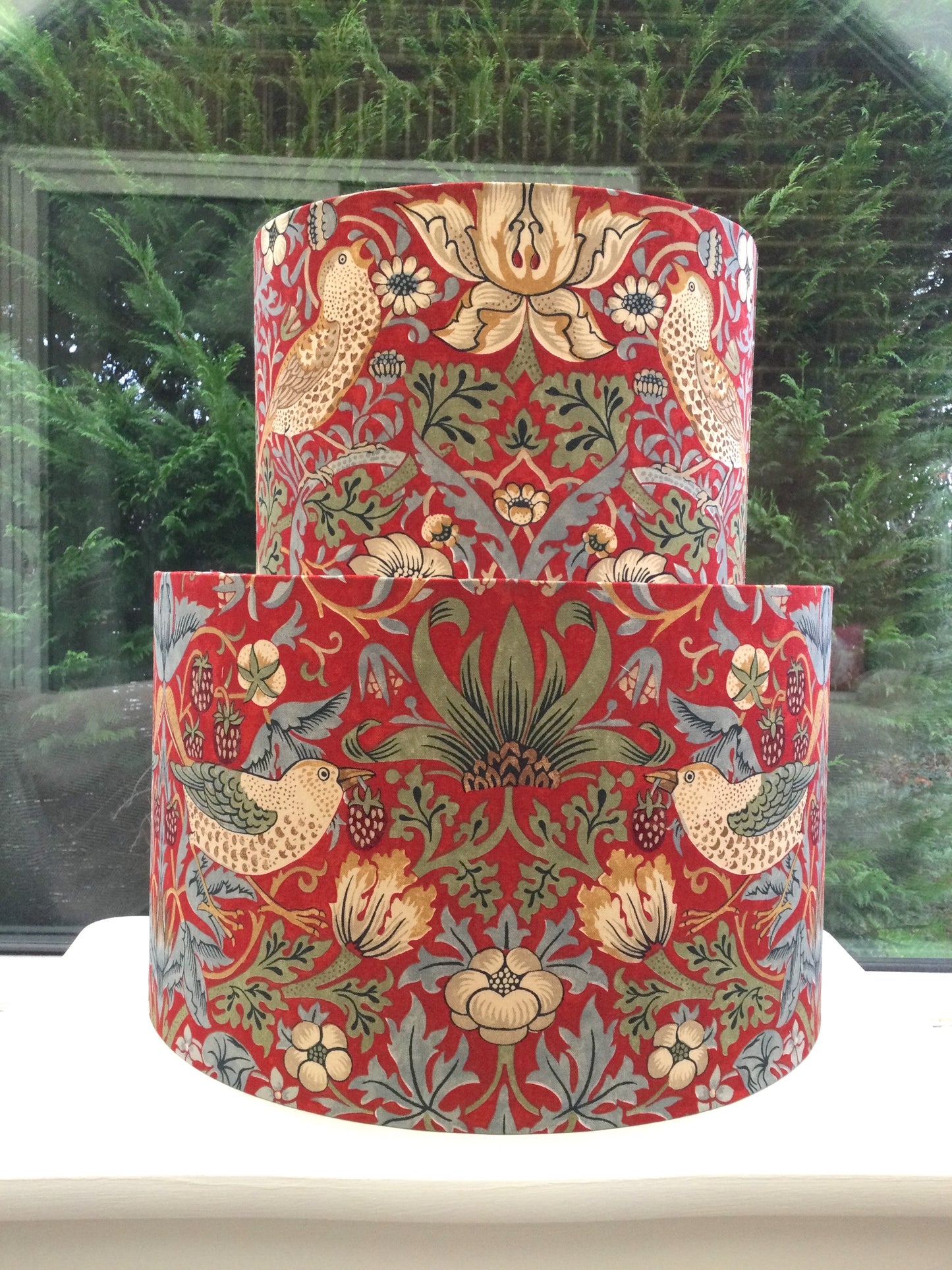 A vibrant red lampshade with intricate William Morris patterns, illuminated from within, casting a warm and inviting glow.