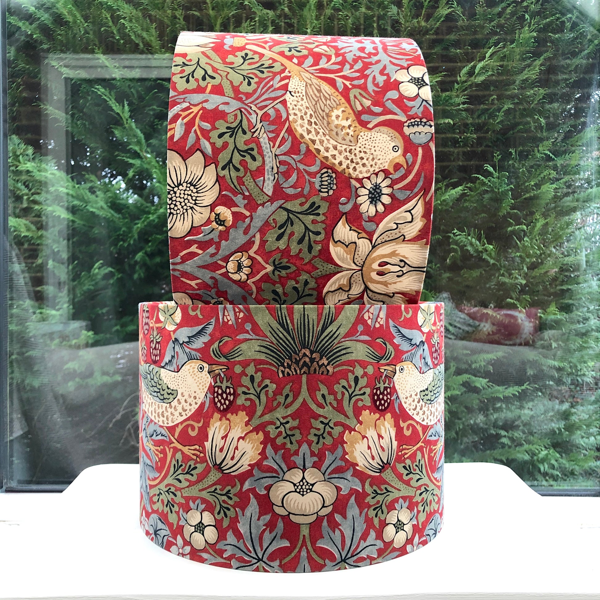 A vibrant red lampshade with intricate William Morris patterns, illuminated from within, casting a warm and inviting glow.