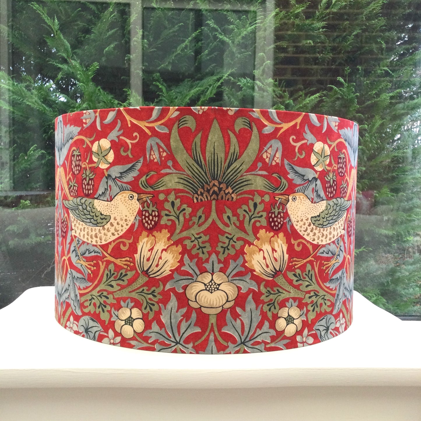 A vibrant red lampshade with intricate William Morris patterns, illuminated from within, casting a warm and inviting glow.