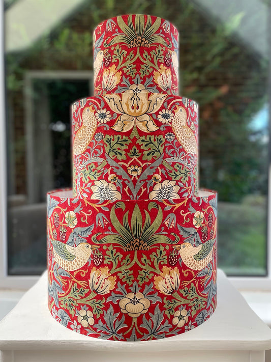 A vibrant red lampshade with intricate William Morris patterns, illuminated from within, casting a warm and inviting glow.